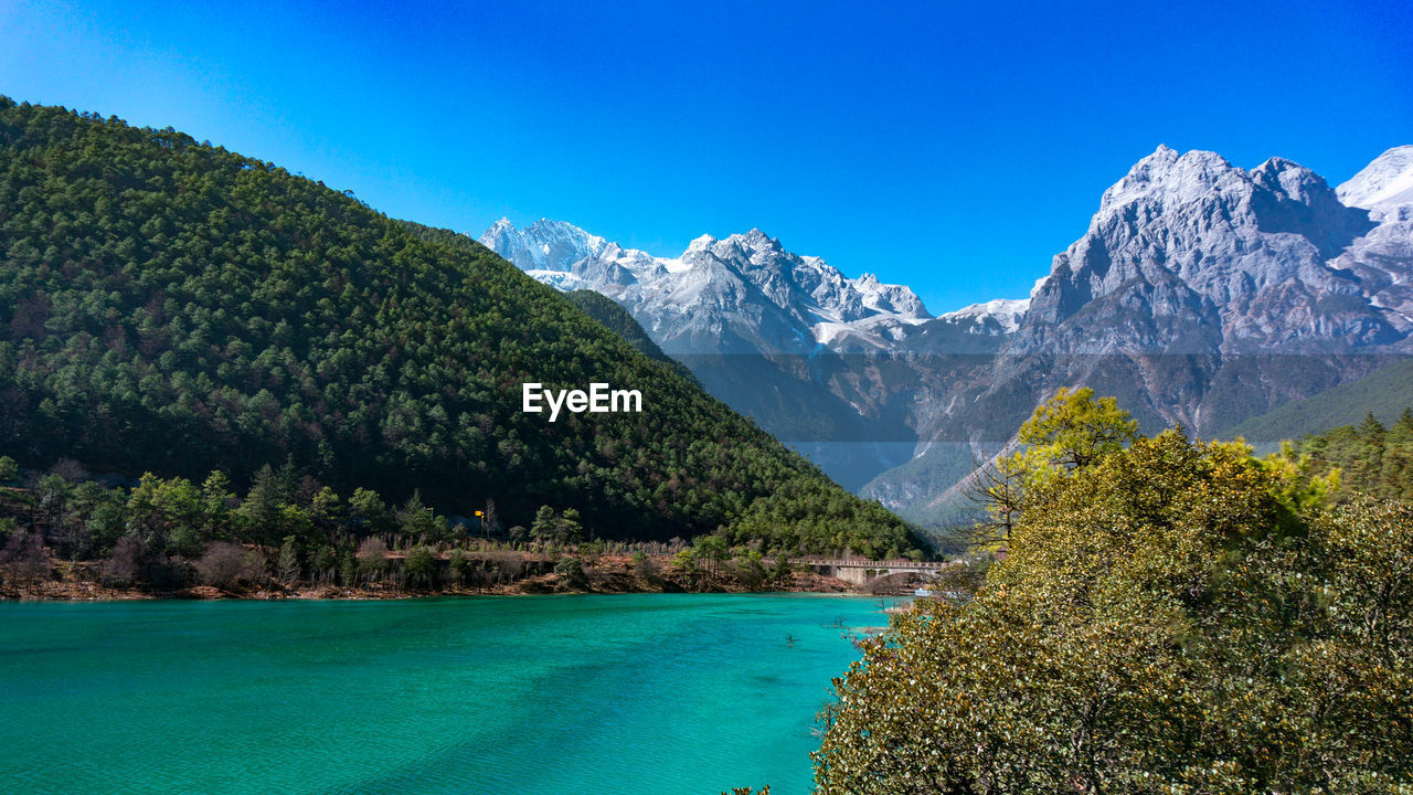 Scenic view of sea and mountains against clear blue sky