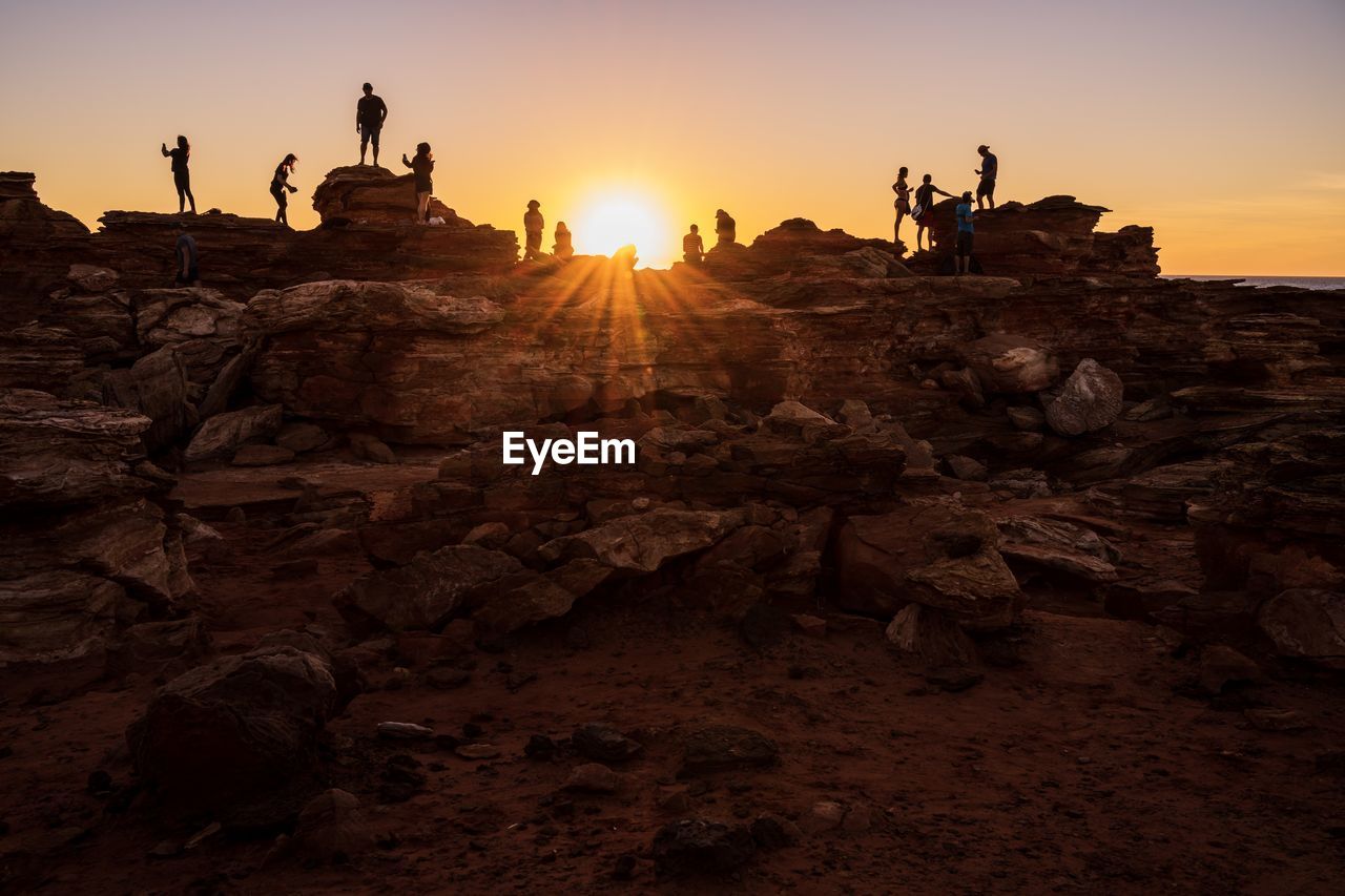 People on rock formation against sky during sunset