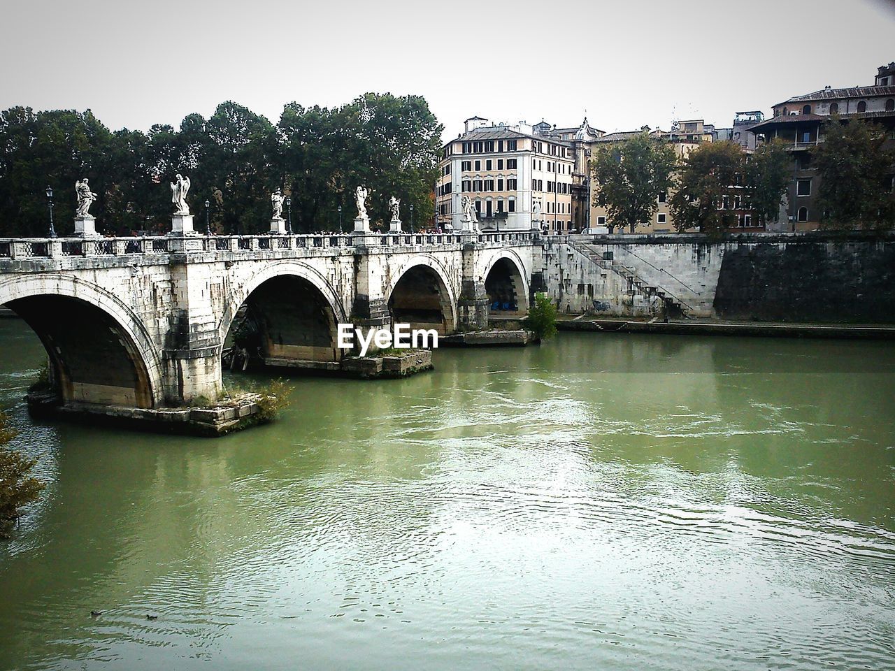 Bridge over river by buildings against sky