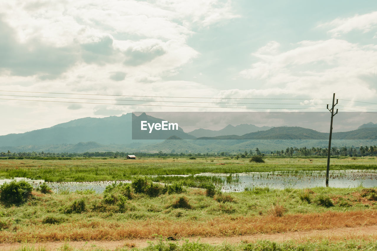 Scenic view of field and water source with mountains, hills and valleys against sky