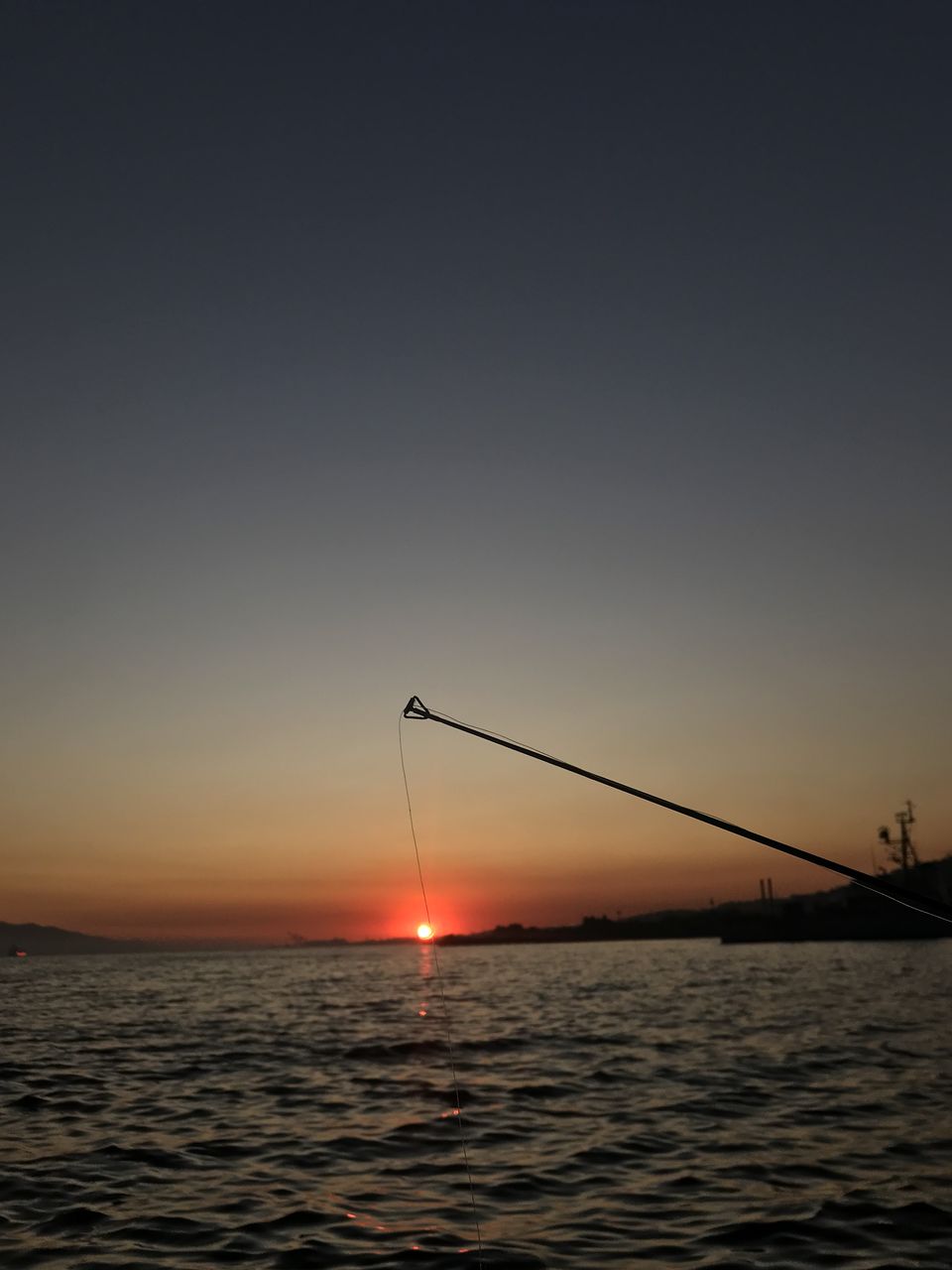 SILHOUETTE OF FISHING ROD OVER SEA AGAINST SKY DURING SUNSET
