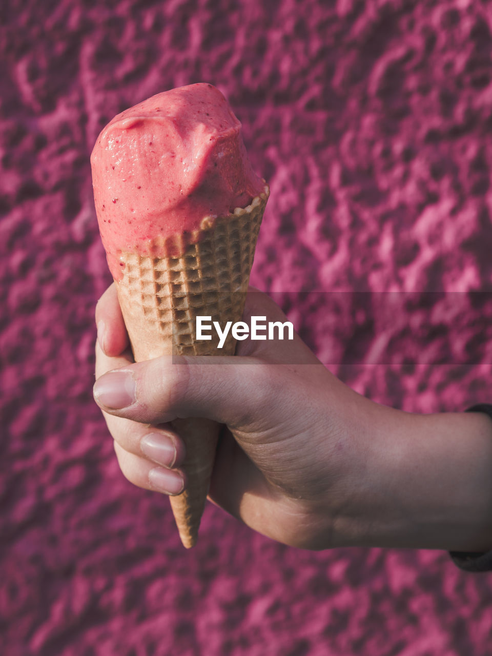 Cropped hand of boy holding ice cream cone against wall