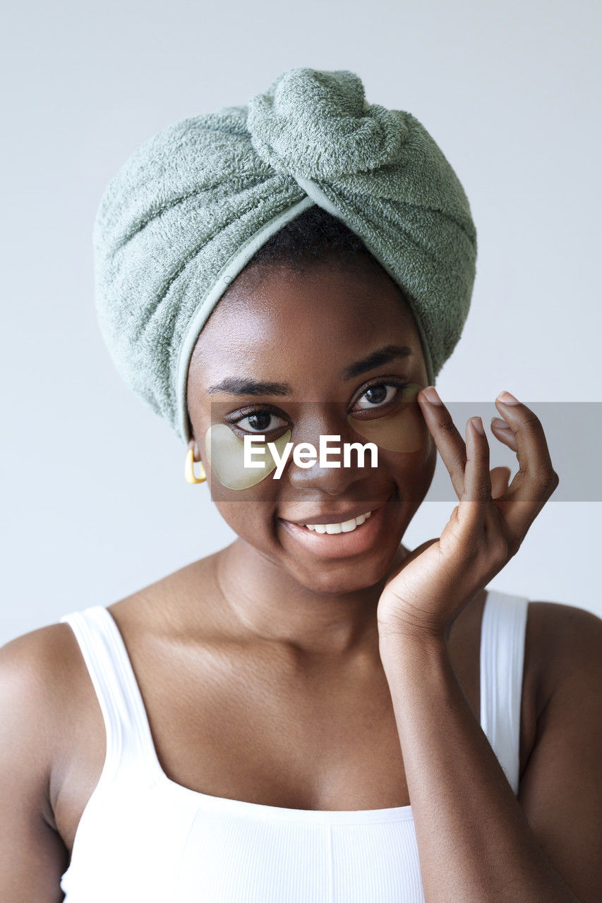 Happy young woman wearing towel on head in front of wall