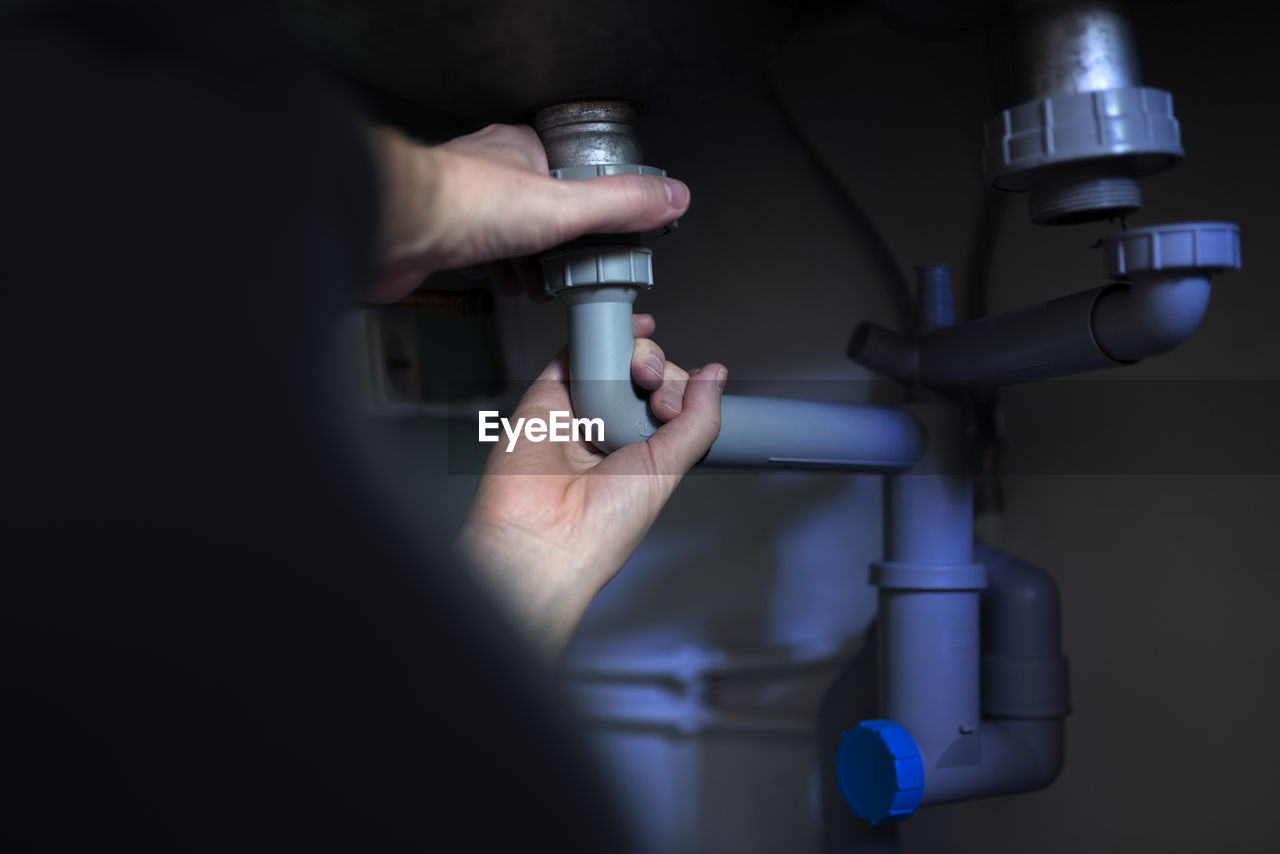 Hands of man fixing pipe under bathroom sink