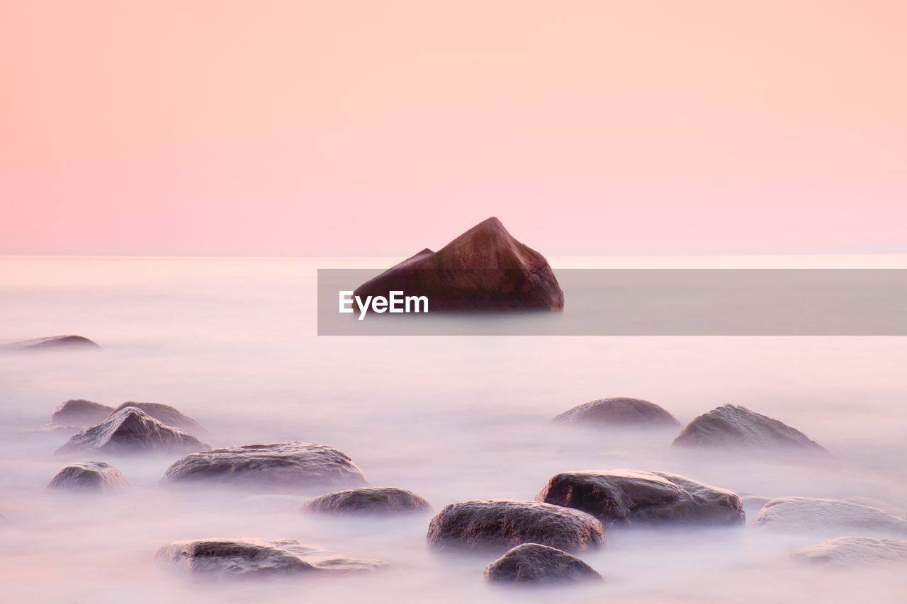 ROCKS IN SEA AGAINST SUNSET SKY