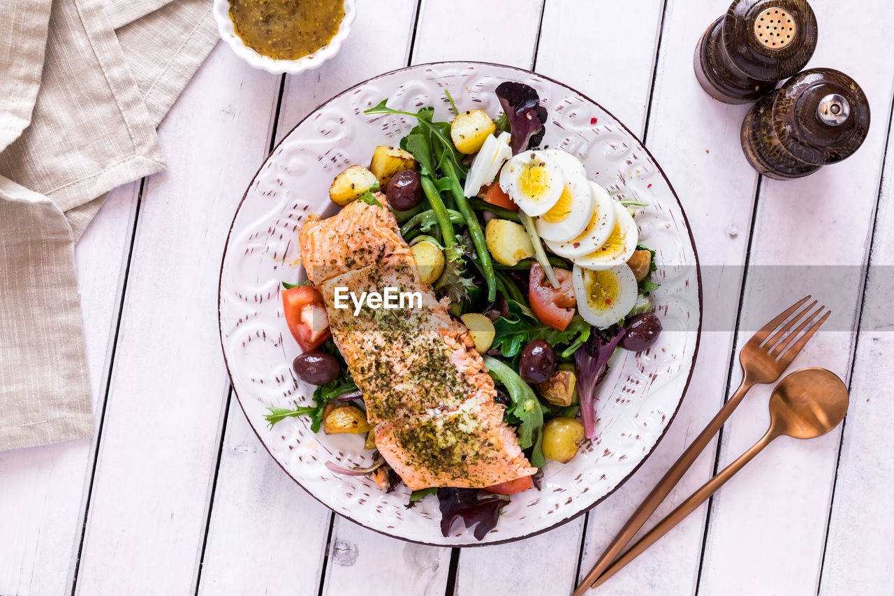 A top down view of a salmon nicoise salad on a rustic table, ready for eating.