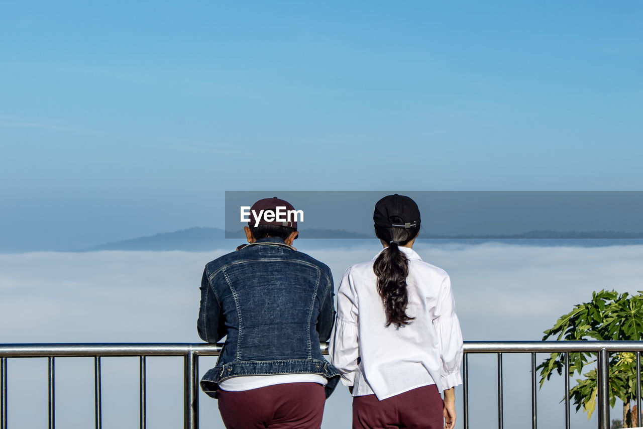 Rear view of couple standing by railing against sky