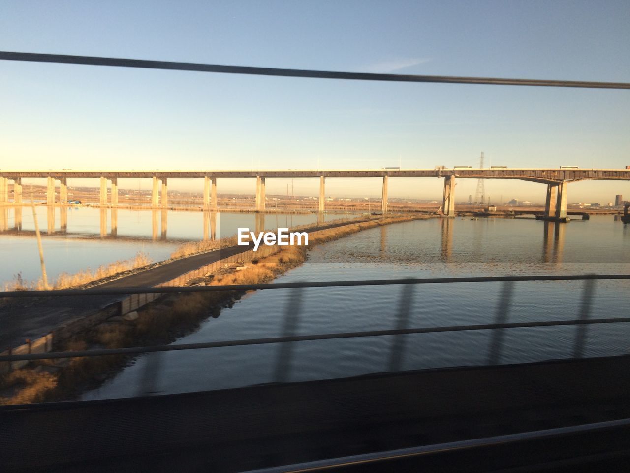 Bridge over river seen through moving train against sky