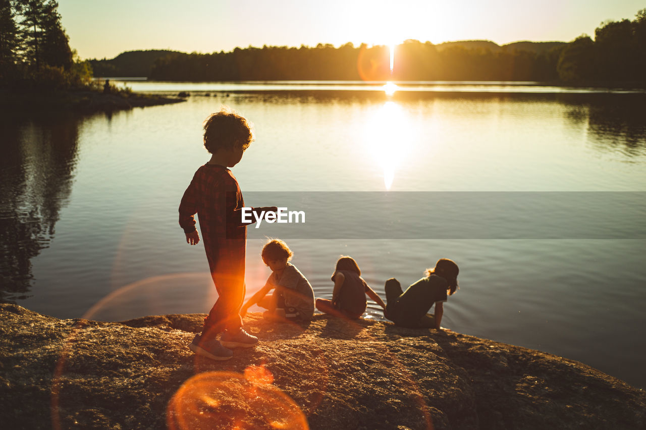 Friends sitting by lake against sky during sunset