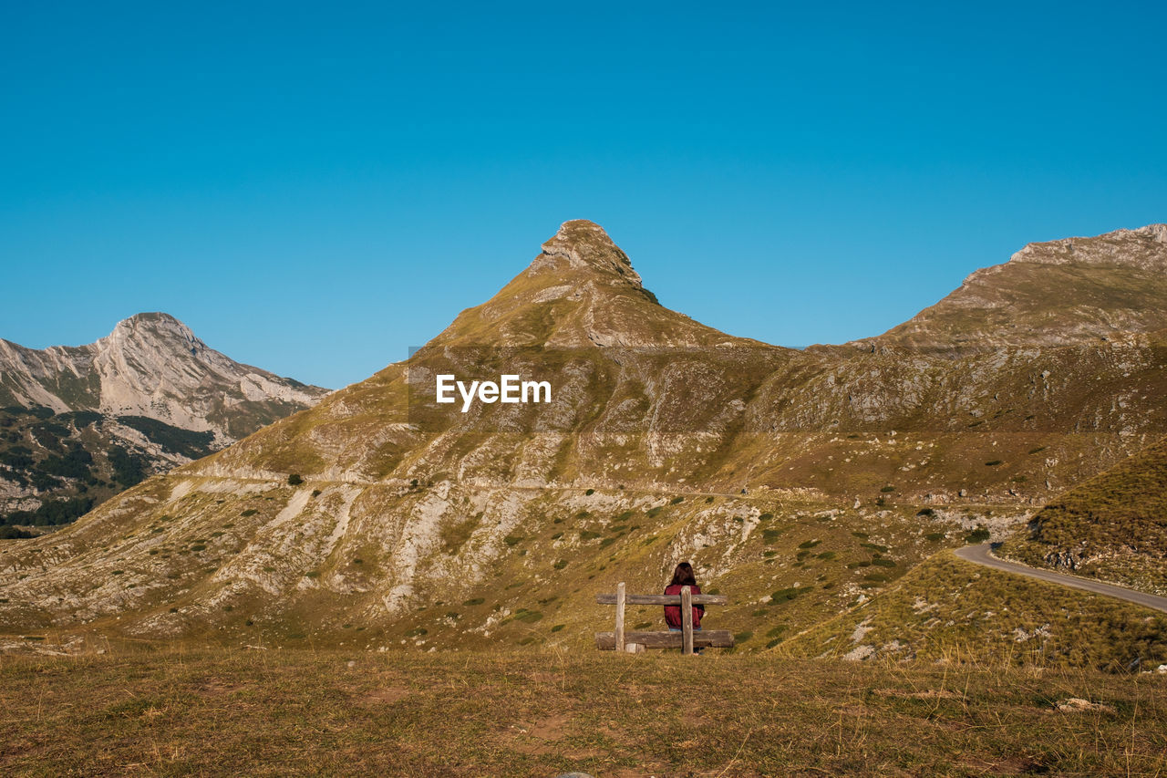 MAN STANDING ON MOUNTAIN ROAD AGAINST CLEAR SKY