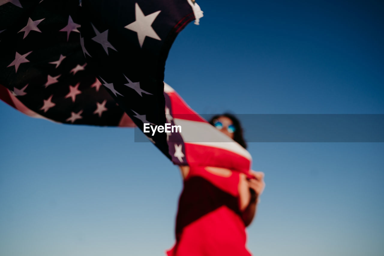 Low angle view of woman with american flag against clear blue sky