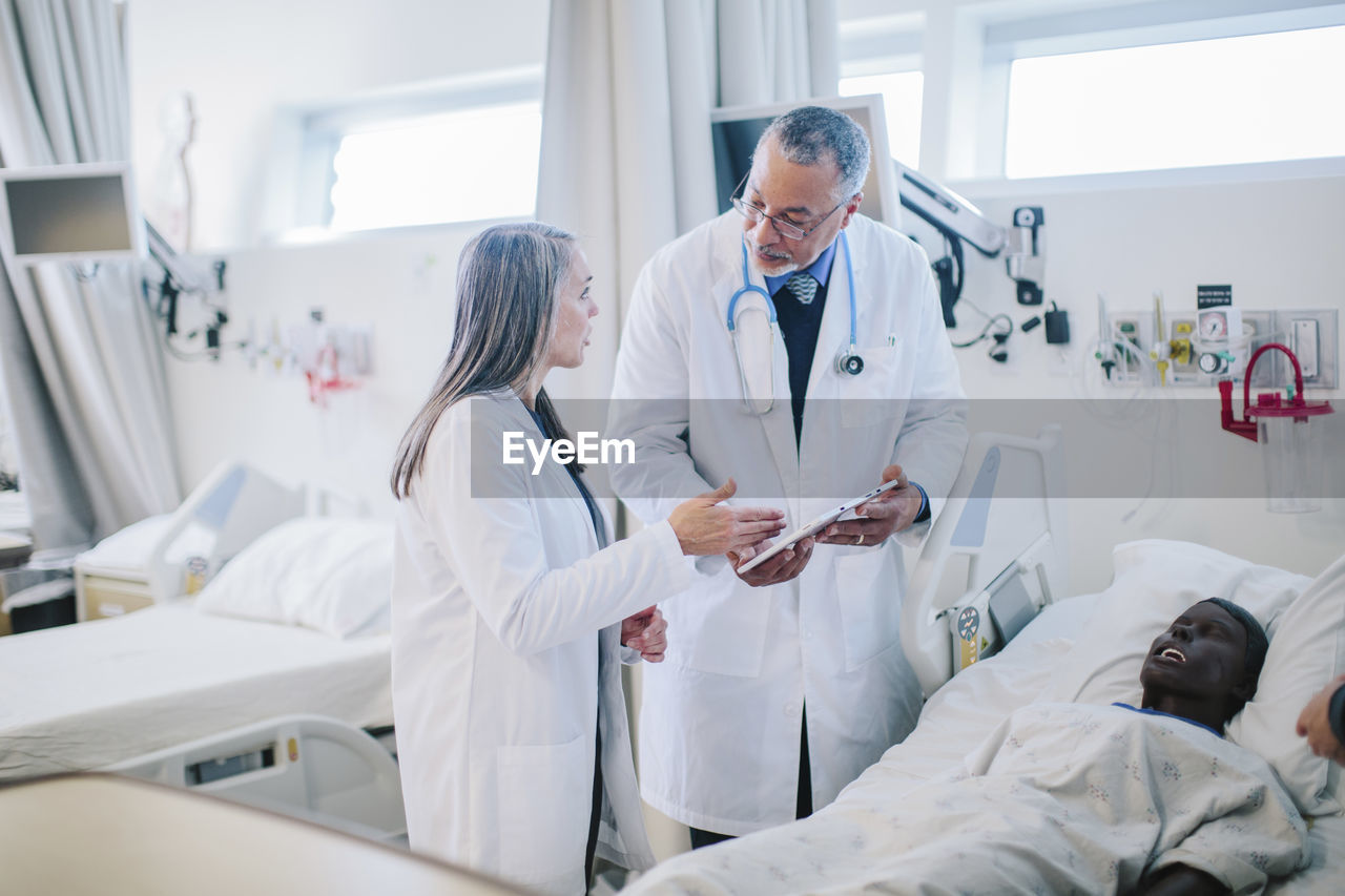 Male doctor discussing with female coworker over tablet computer in hospital ward