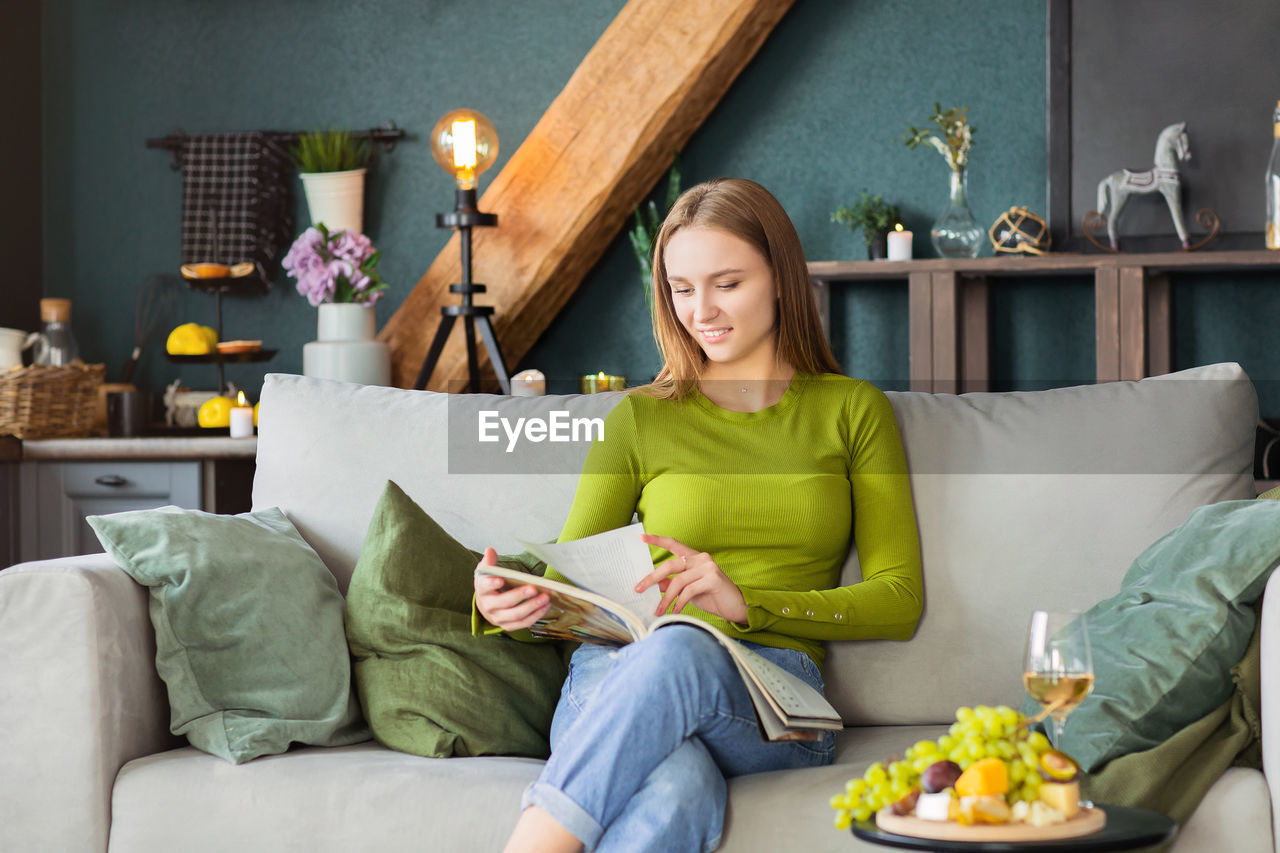 Young woman reading book while sitting on sofa