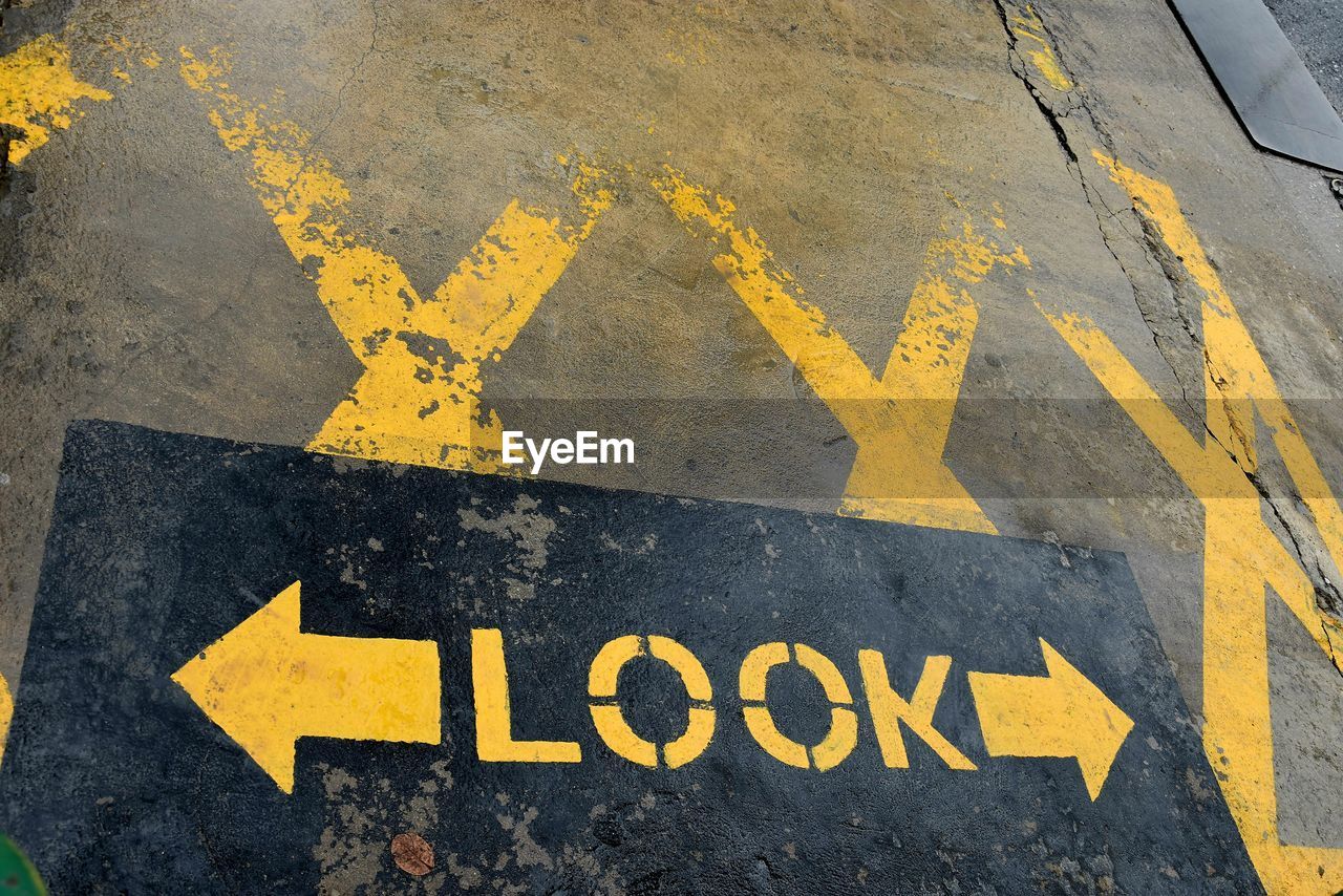 yellow, sign, communication, road, symbol, guidance, text, no people, transportation, road marking, arrow symbol, road surface, western script, marking, asphalt, city, day, lane, road sign, directional sign, high angle view, warning sign, street, wall, outdoors, information sign, art, black, infrastructure, number, close-up