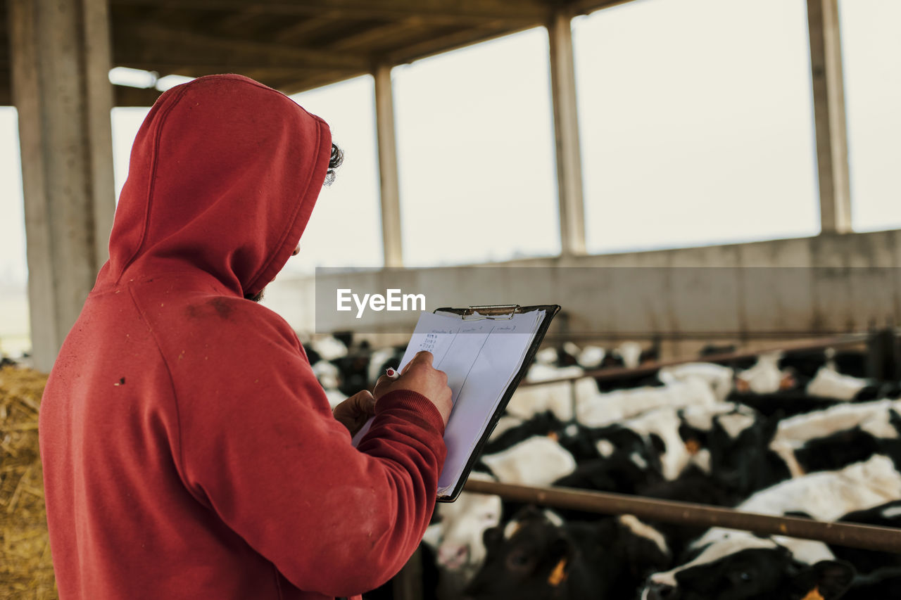 Farmer writing on clipboard while standing at dairy farm