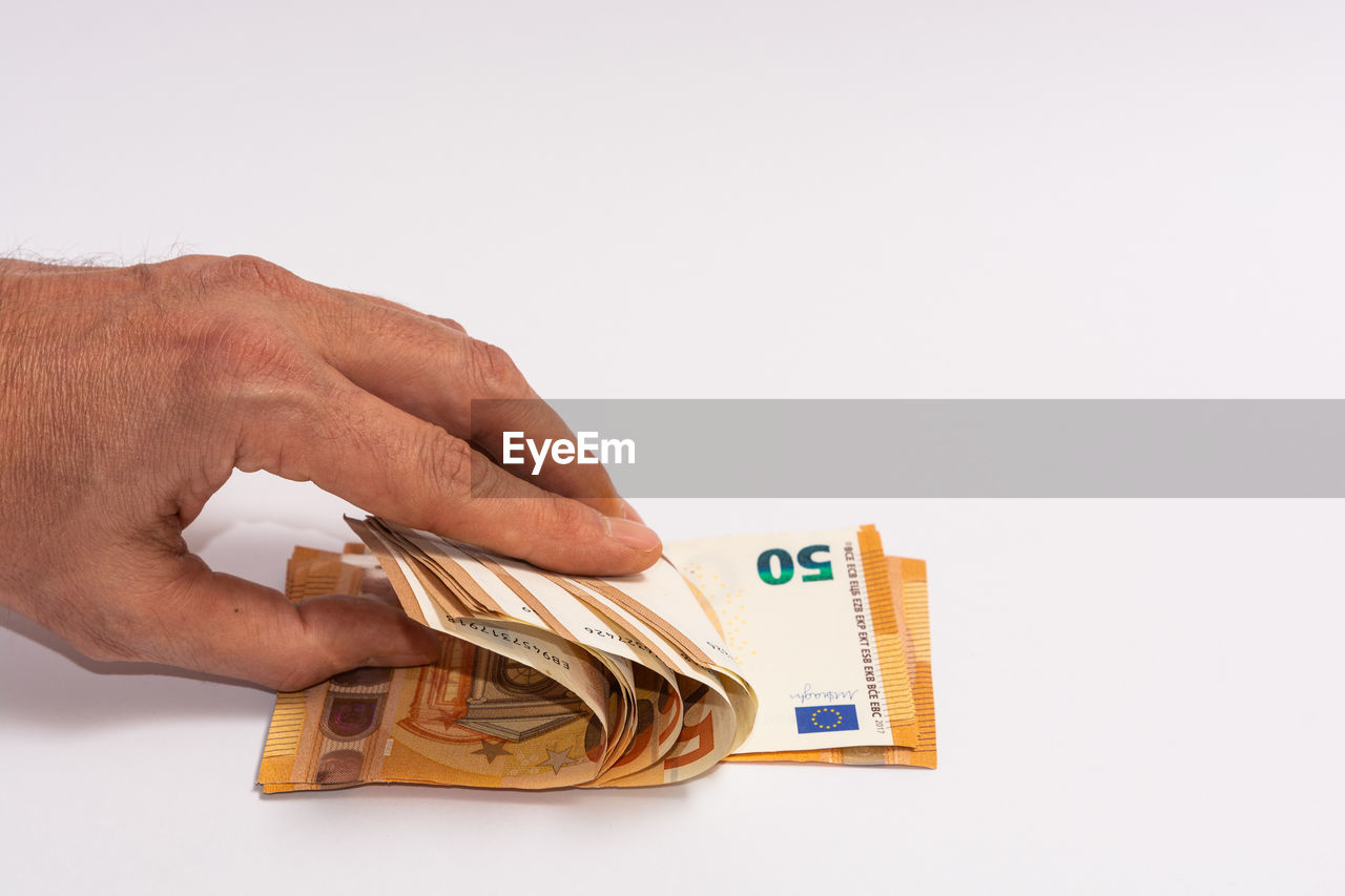 CLOSE-UP OF A HAND HOLDING PAPER OVER WHITE BACKGROUND