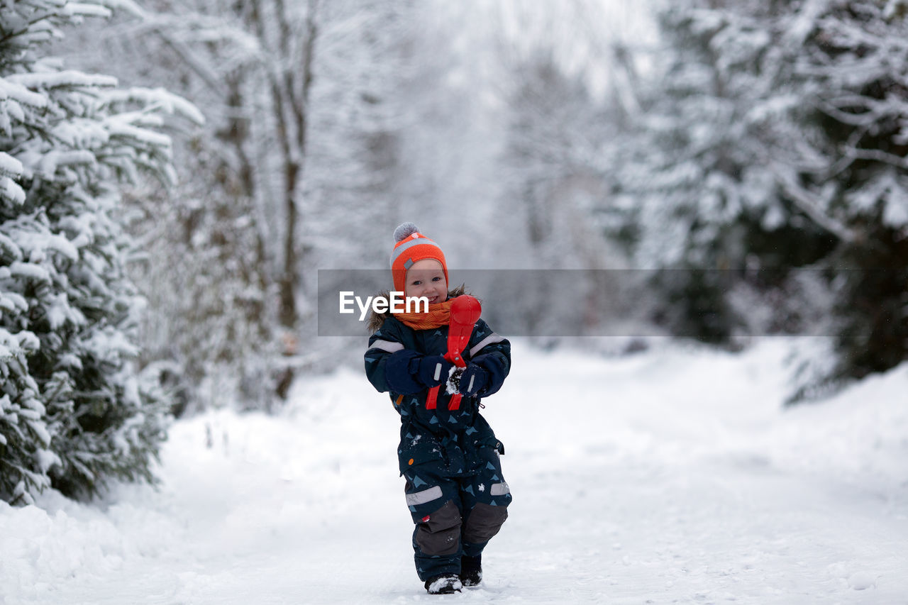 Toddler girl wearing winter clothes having fun outside in snowy day. girl is making snowballs.