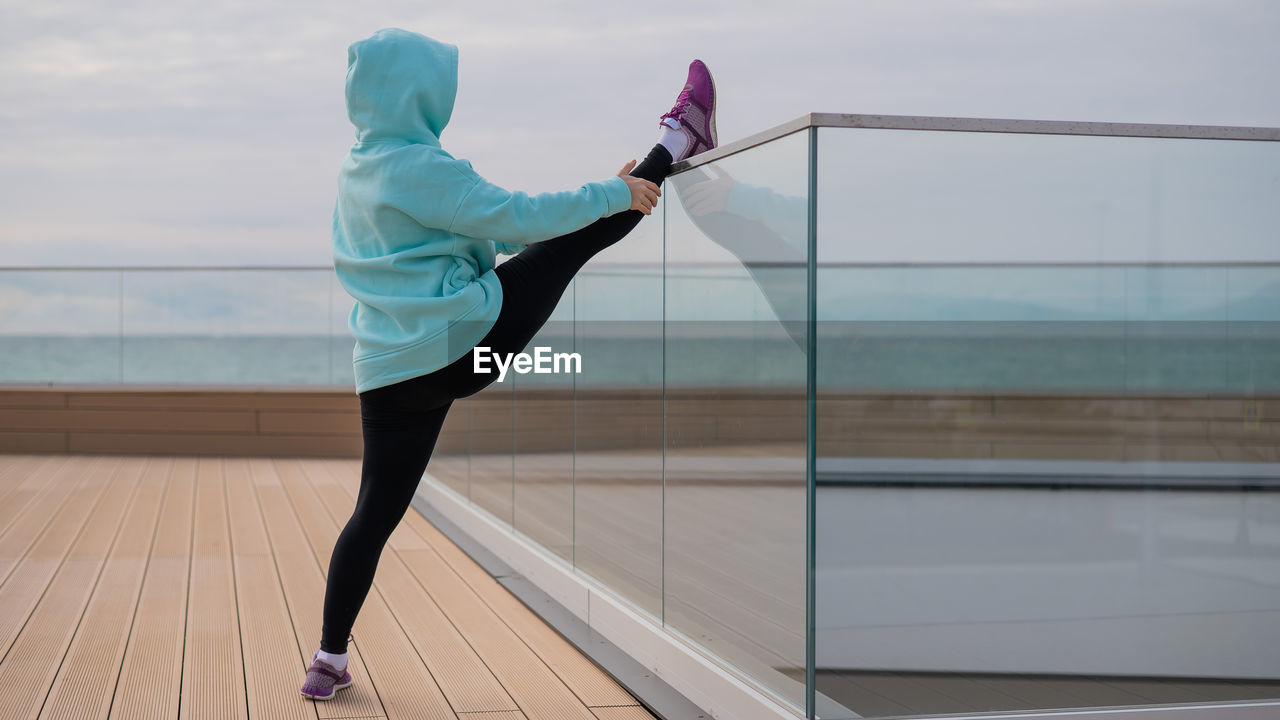 Full length of woman stretching by glass railing