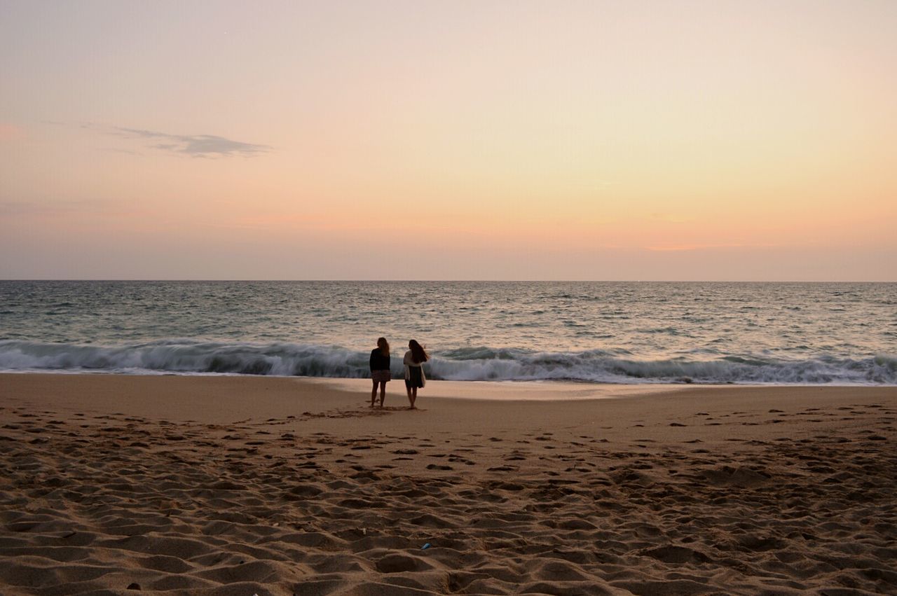 SILHOUETTE FRIENDS STANDING ON BEACH AGAINST SKY DURING SUNSET