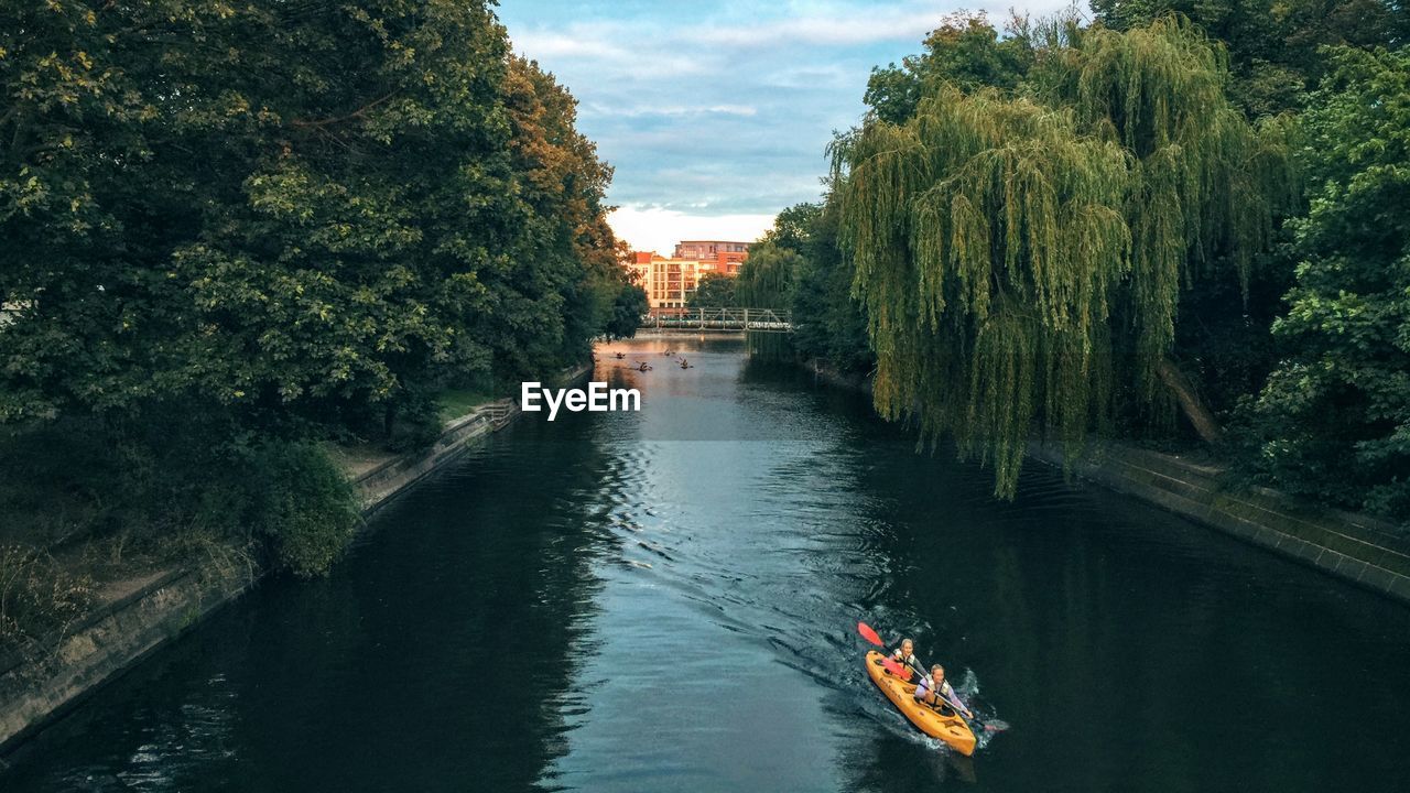 People kayaking on canal amidst trees