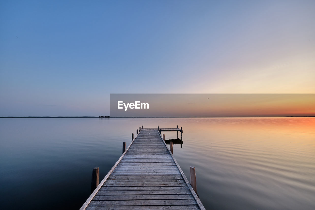 Pier over lake against sky during sunset