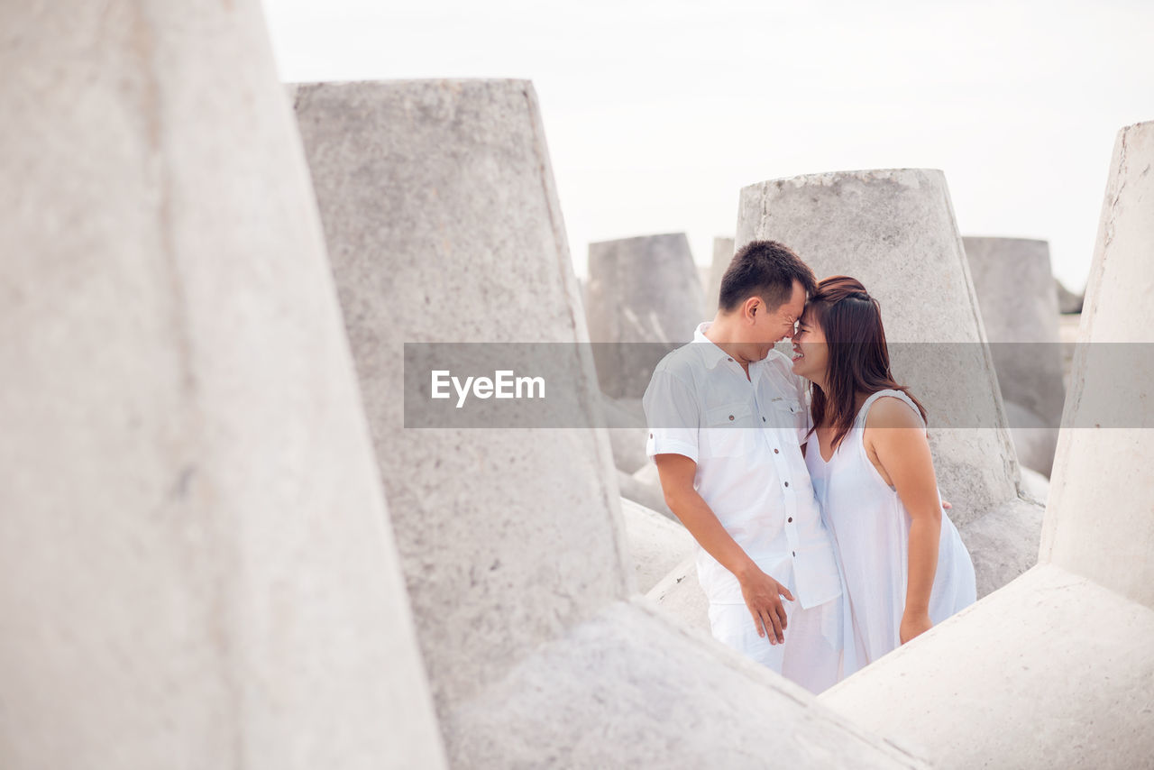 Happy couple standing amidst tetrapod against sky