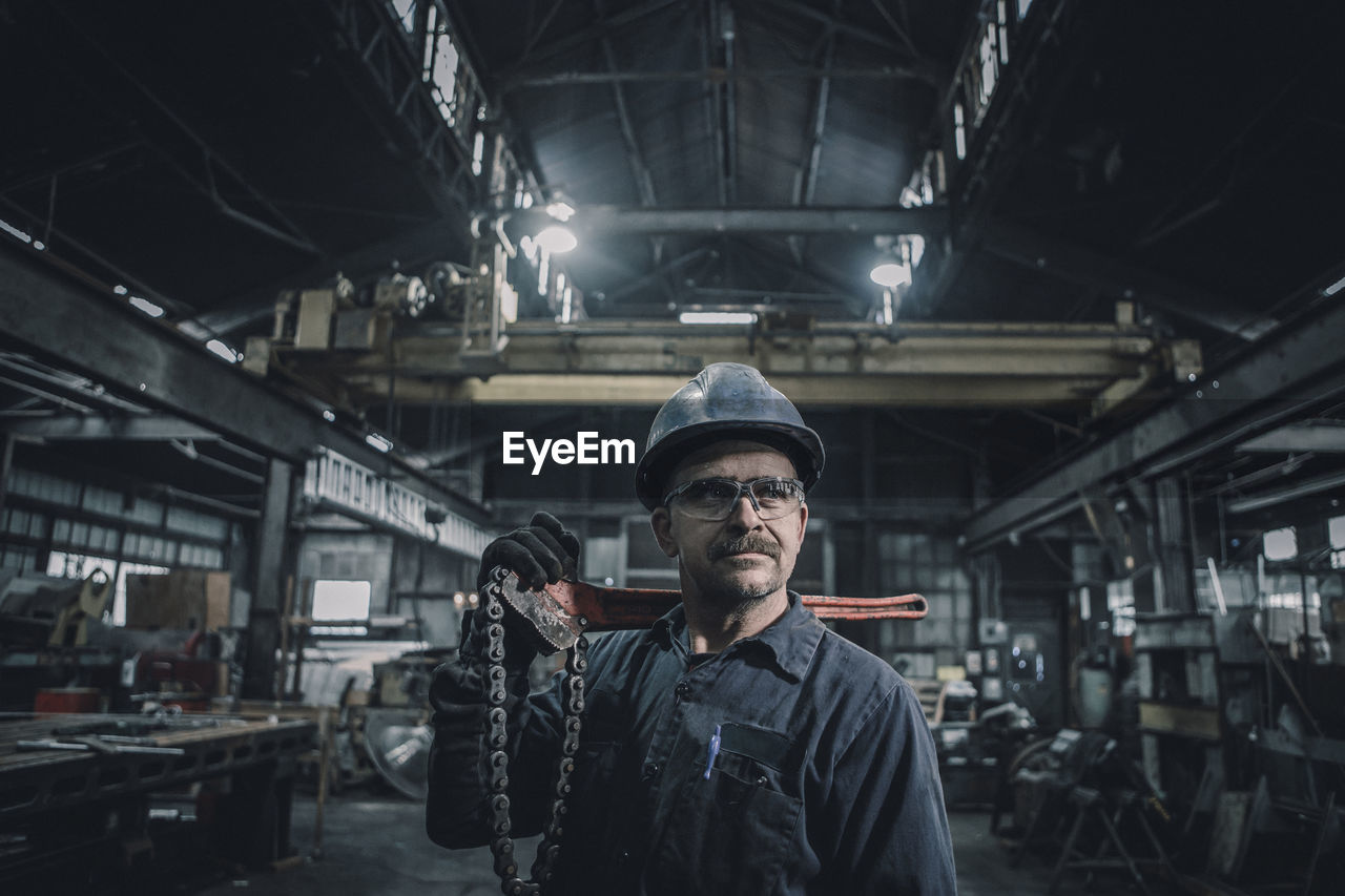 Male worker carrying work tool looking away while standing in factory