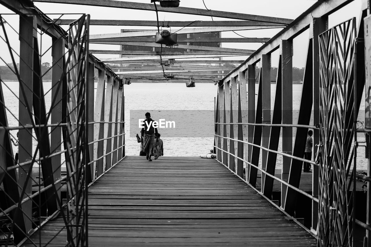 architecture, built structure, the way forward, full length, one person, rear view, bridge, black and white, transportation, monochrome, railing, men, lifestyles, day, monochrome photography, black, adult, nature, walking, leisure activity, diminishing perspective, transport, outdoors, walkway, sky, women, white, footbridge, water, footpath, urban area, travel, line