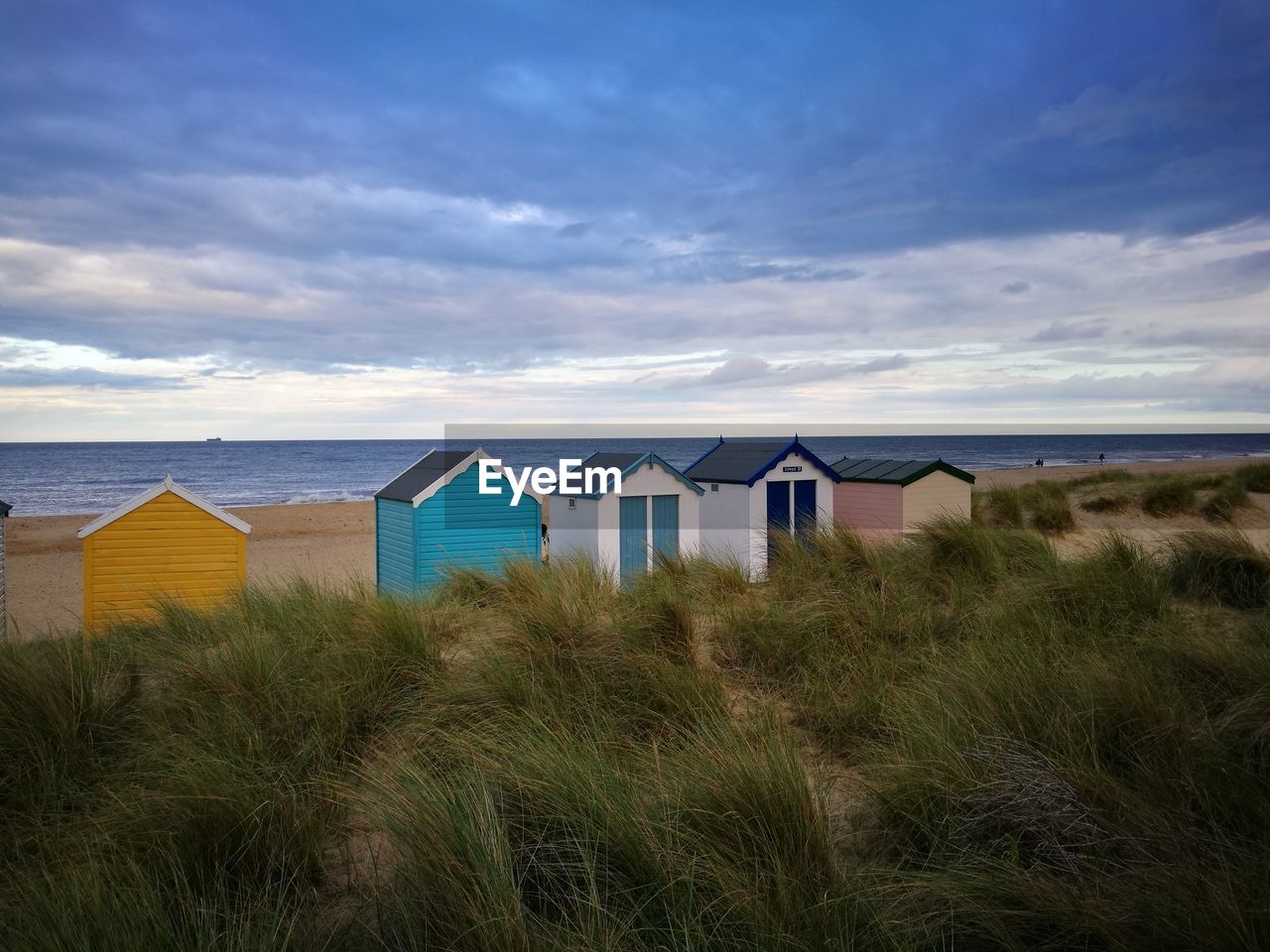 Huts on grassy beach against cloudy sky