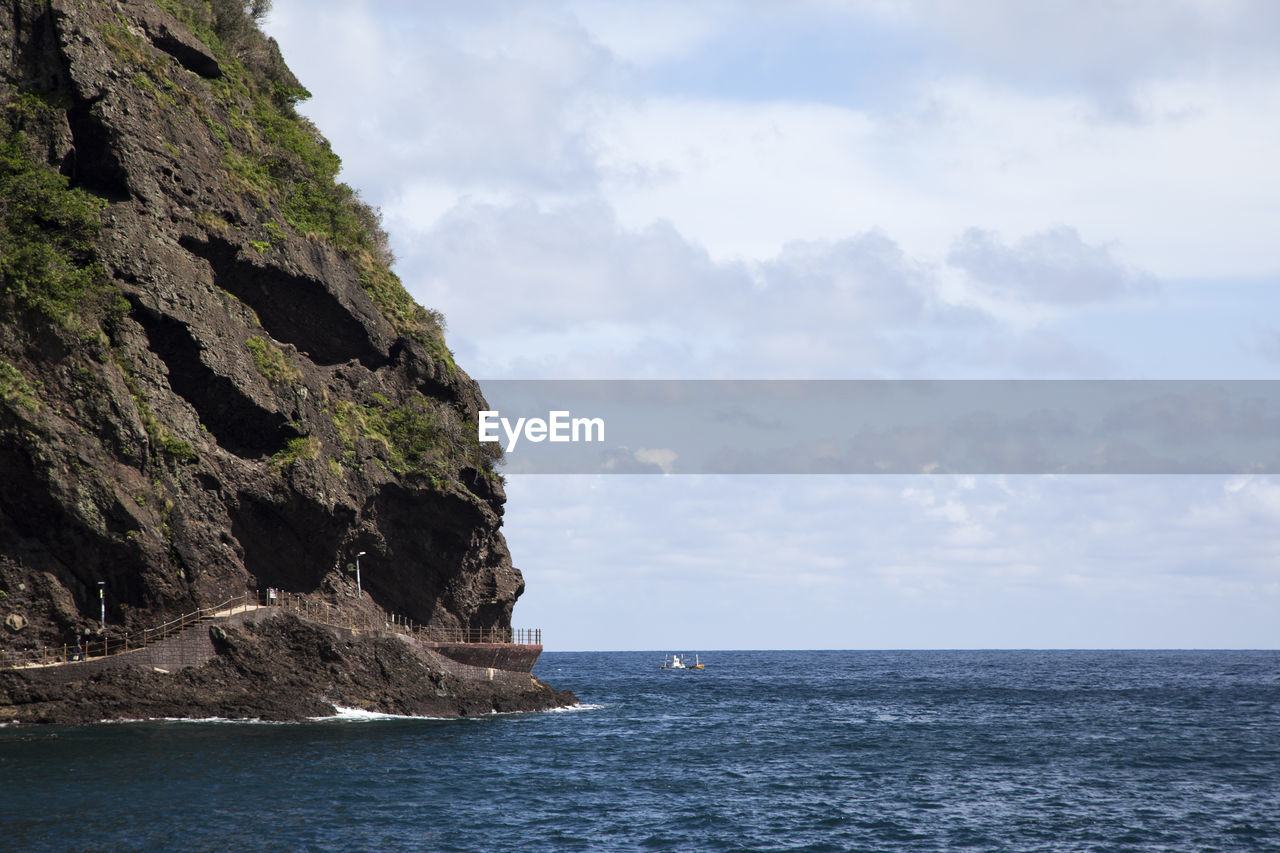 Scenic view of mountain at sea shore against cloudy sky