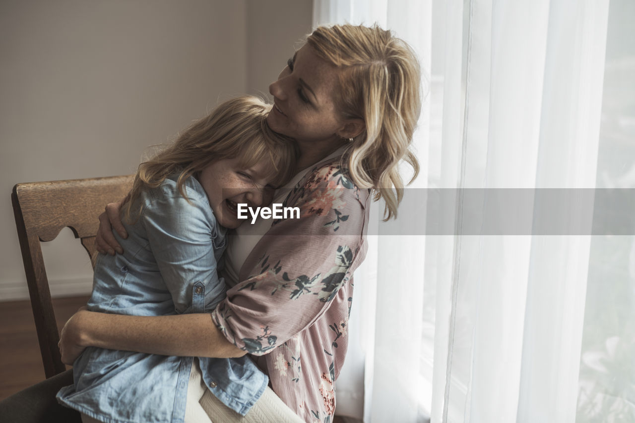 Mother and daughter laughing close together in natural light studio