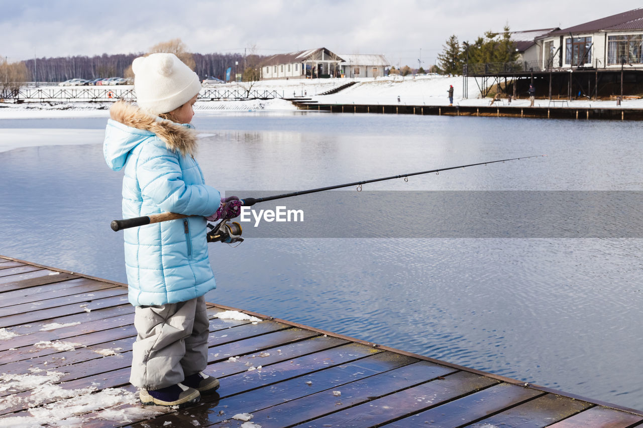 REAR VIEW OF WOMAN WITH FISHING ROD STANDING IN LAKE