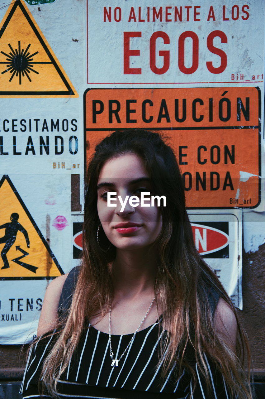 Portrait of smiling young woman standing against posters