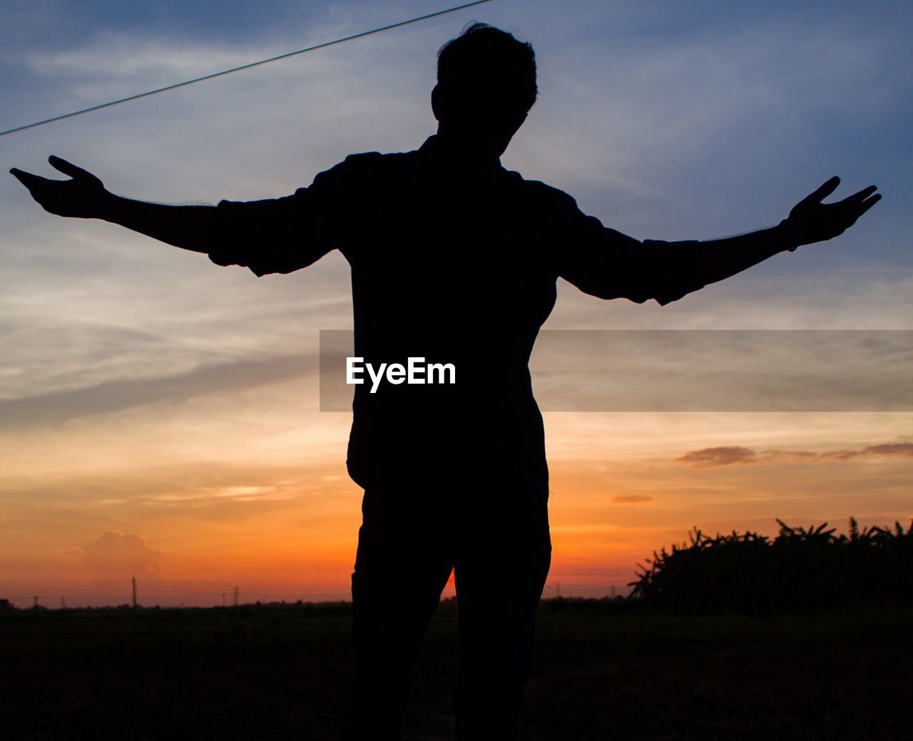 SILHOUETTE MAN STANDING ON FIELD AT SUNSET