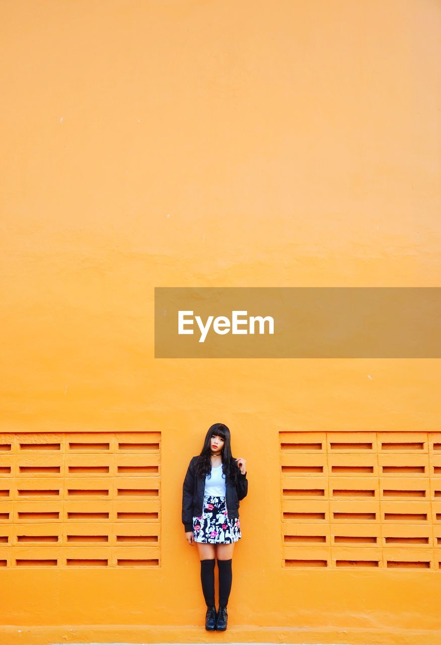 Full length of woman standing against orange wall