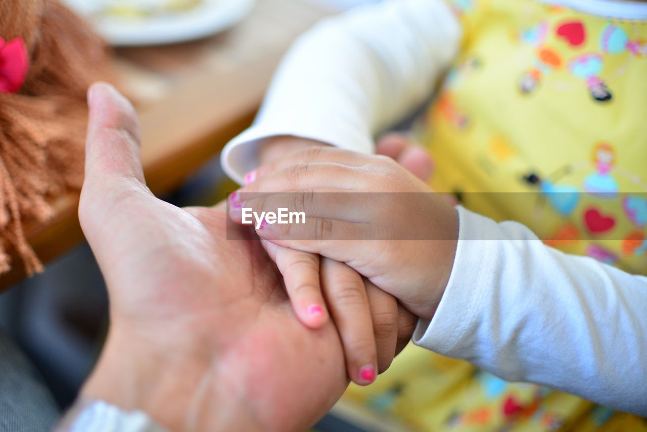 Midsection of baby girl holding mother hand at home