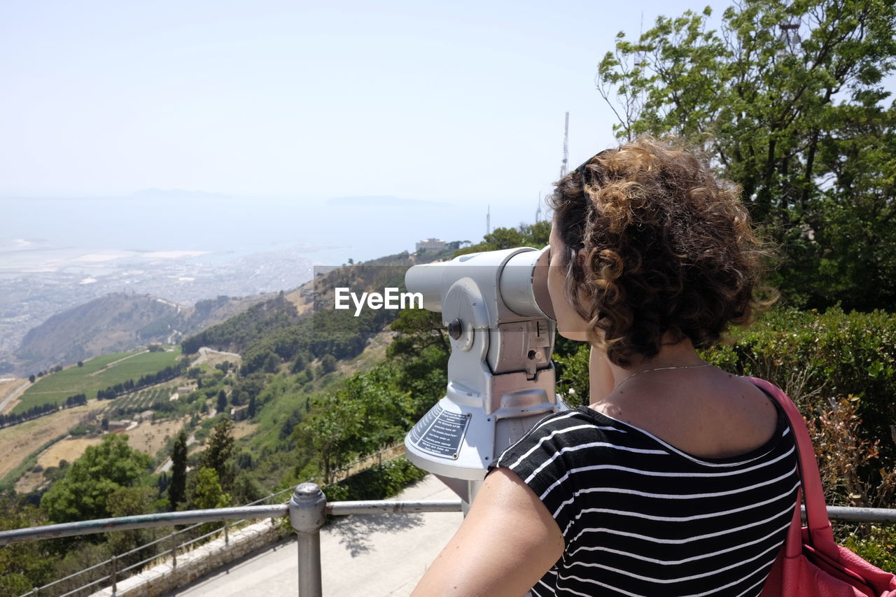 Rear view of woman looking through coin-operated binoculars from observation point at erice