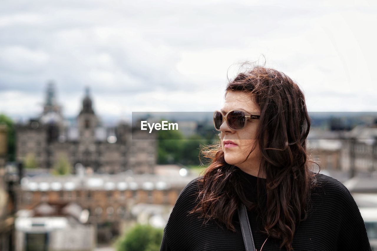 Close-up of woman wearing sunglasses looking away standing against cityscape