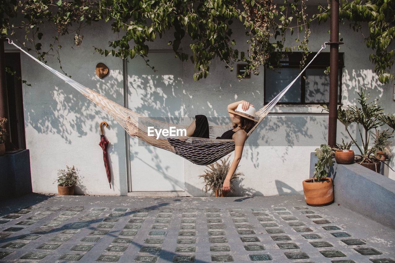 Woman relaxing in hammock against wall at yard