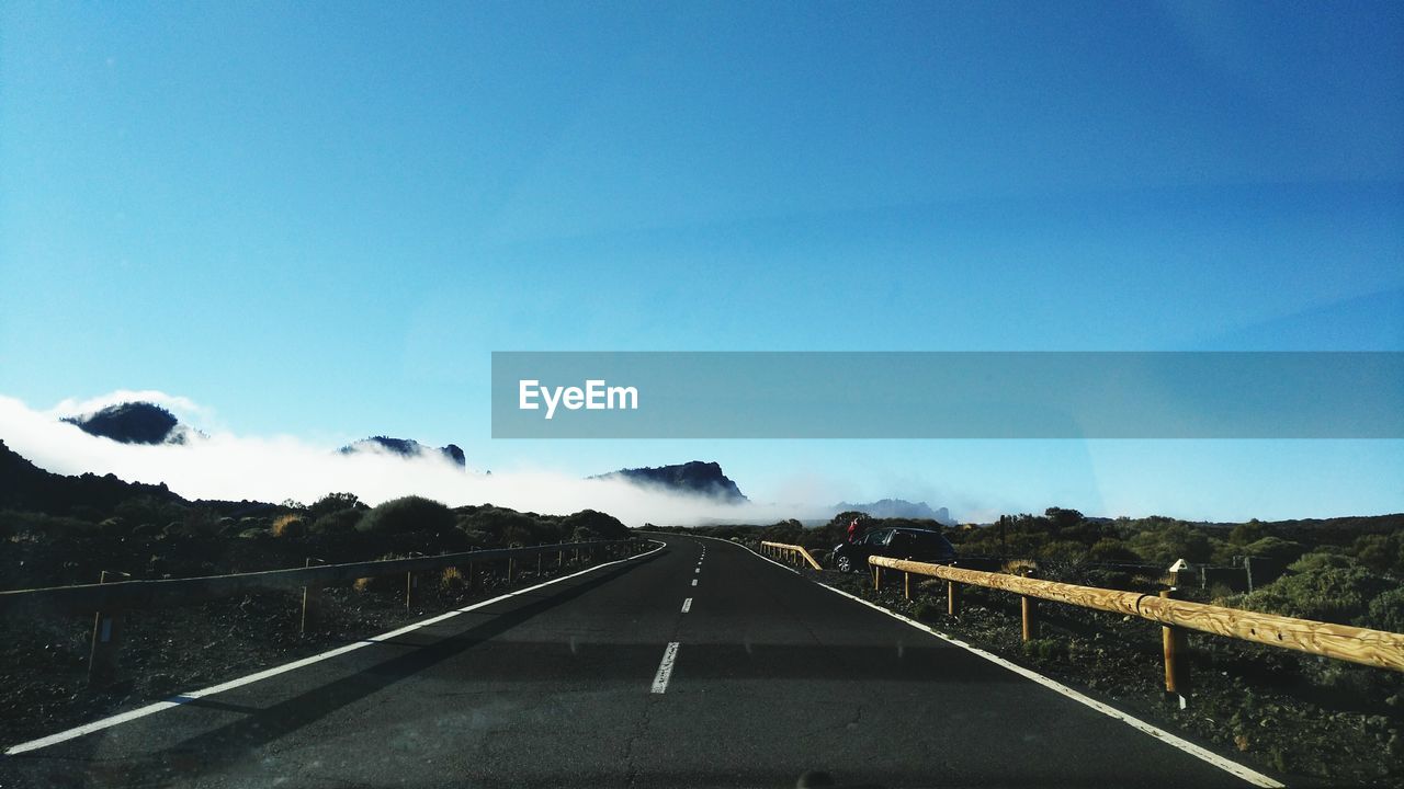 Road amidst field against blue sky