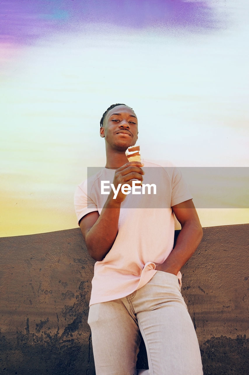 PORTRAIT OF SMILING YOUNG MAN STANDING AGAINST SKY