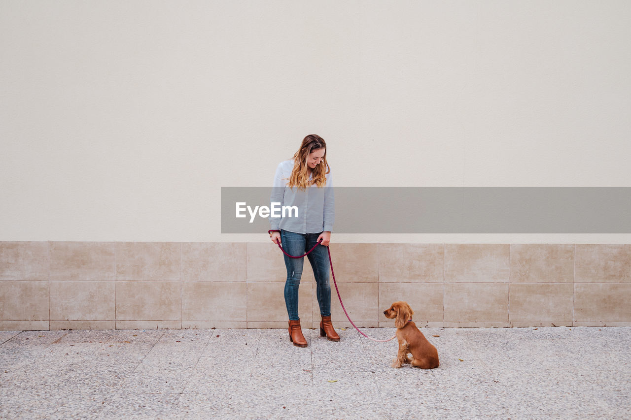 Full length of woman with dog standing on footpath