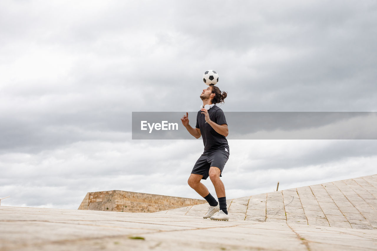 Man training with soccer ball against cloudy sky