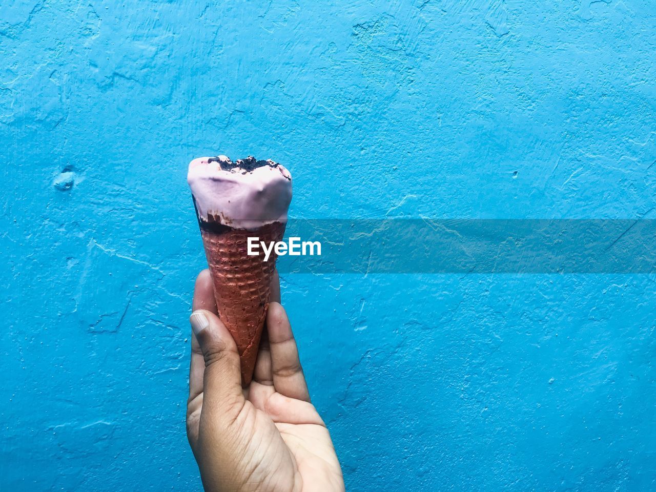 MIDSECTION OF PERSON HOLDING ICE CREAM ON BLUE TABLE