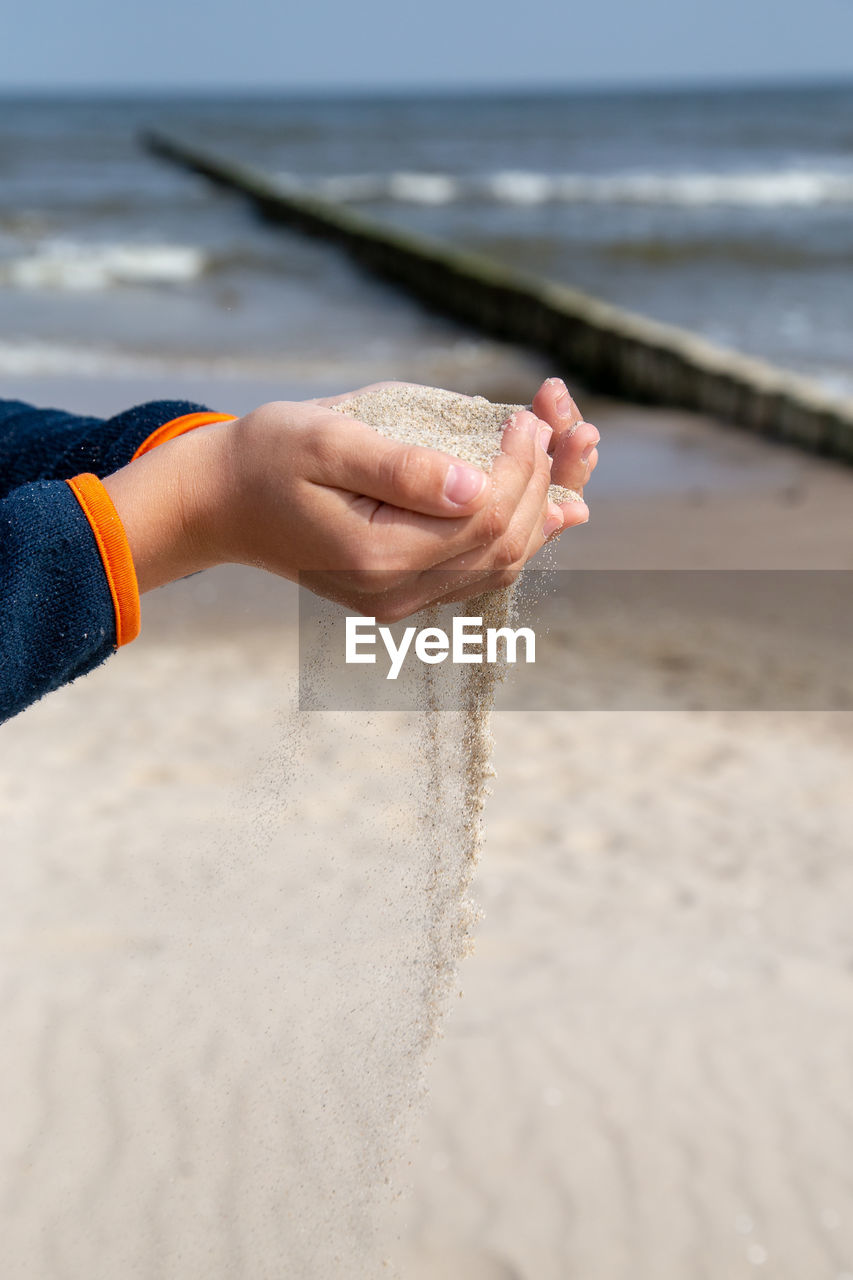 Cropped image of person holding sand at beach