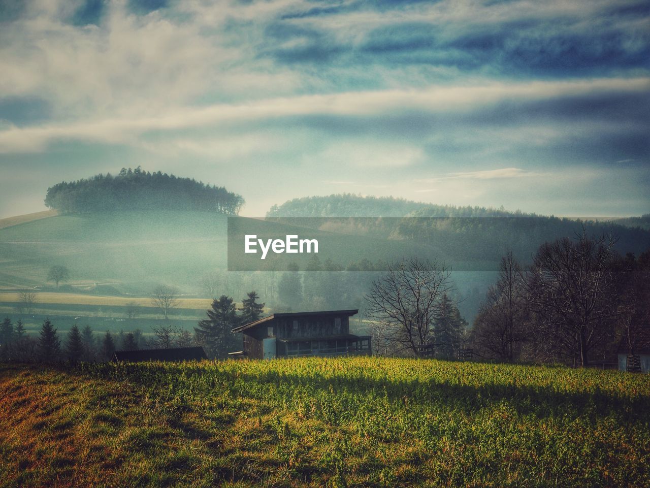 Barn on grassy field against sky during foggy weather