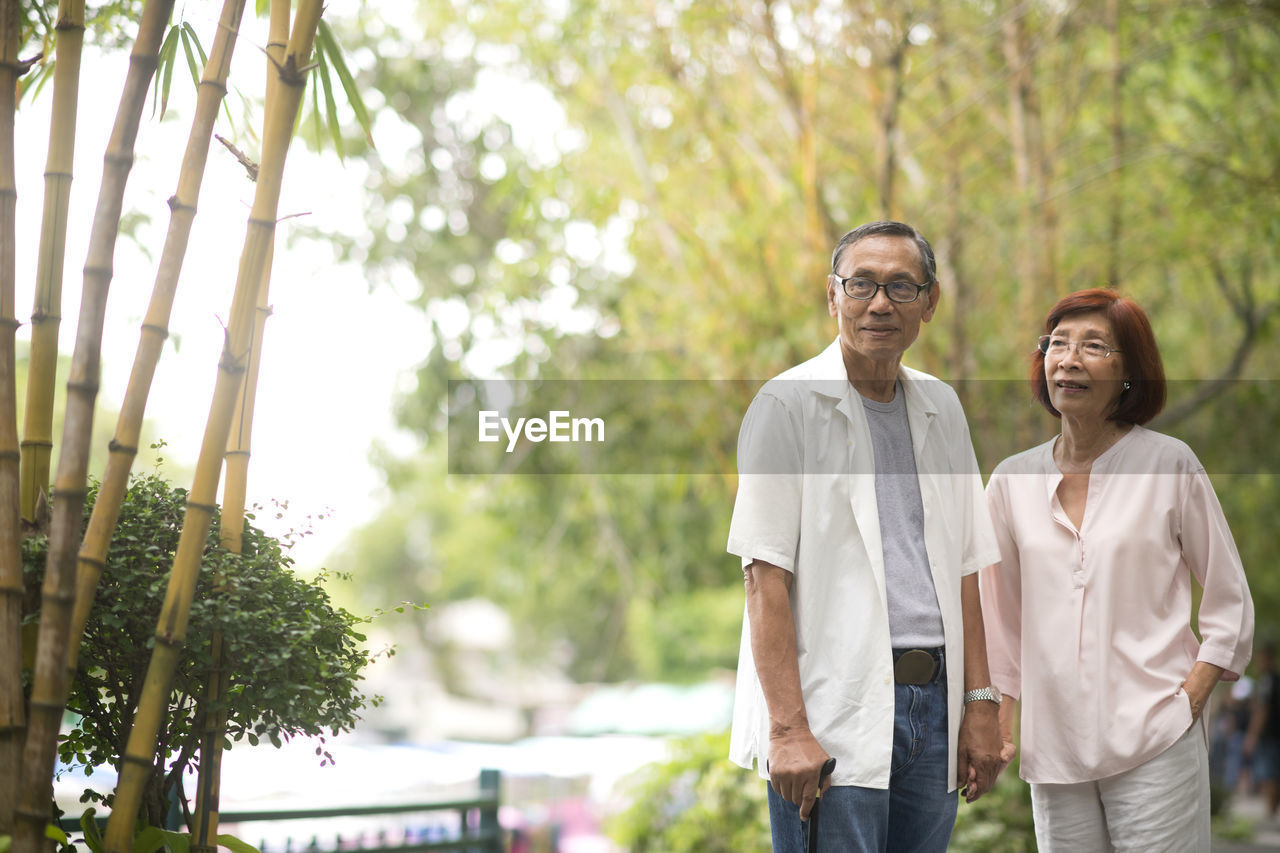 Senior couple standing by railing against trees