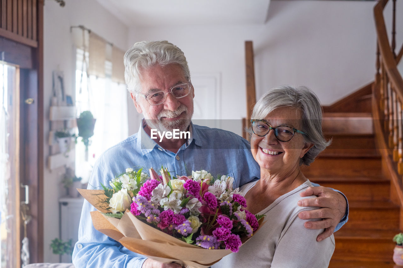 Portrait of smiling couple holding bouquet at home