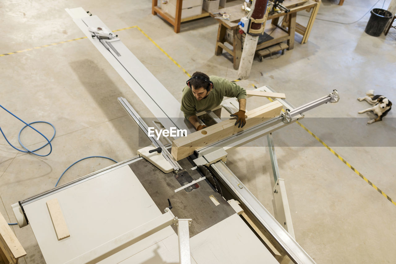 Male carpenter working with wood material at table saw in workshop