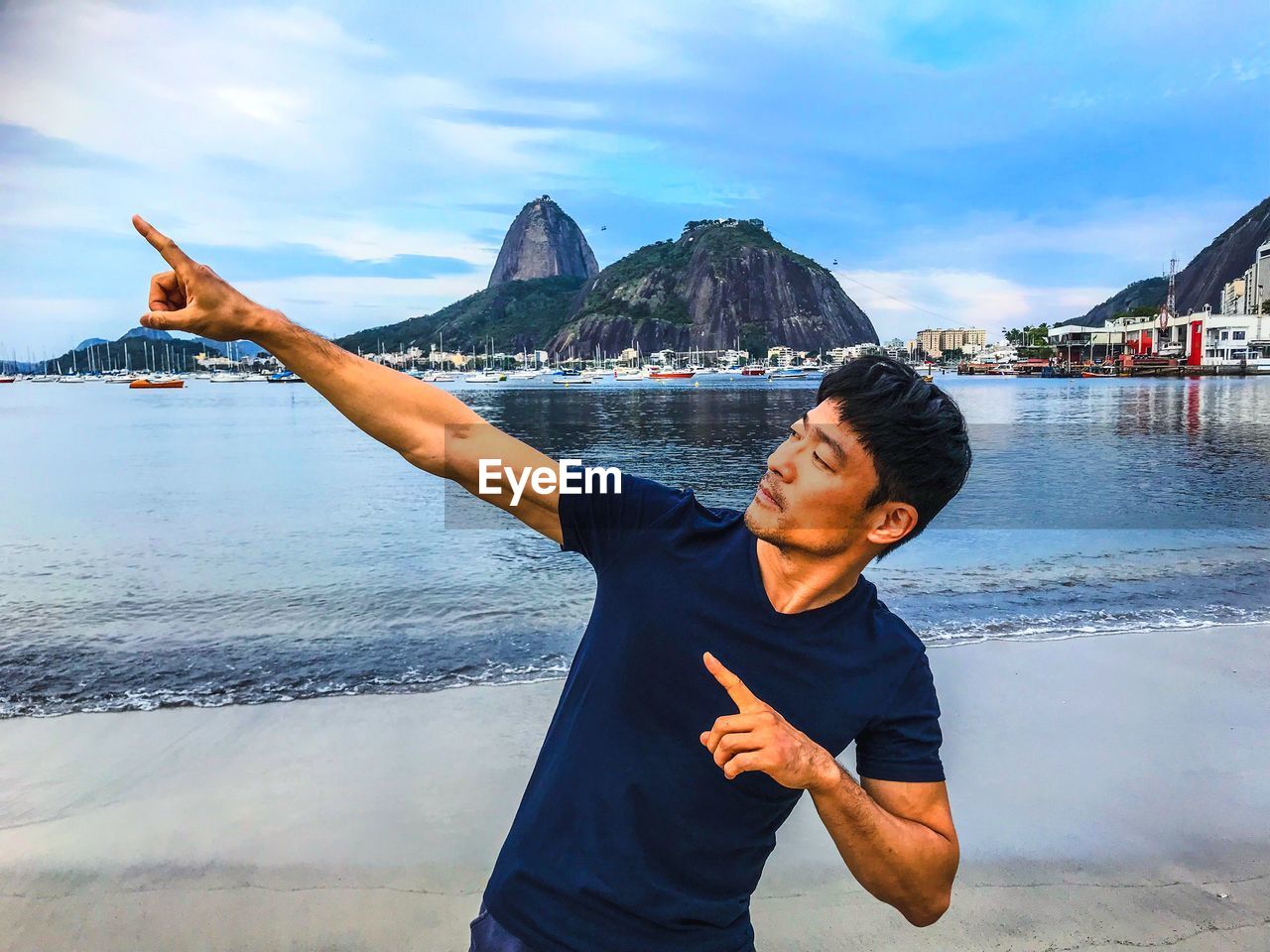 Mature man gesturing while standing at beach against sky